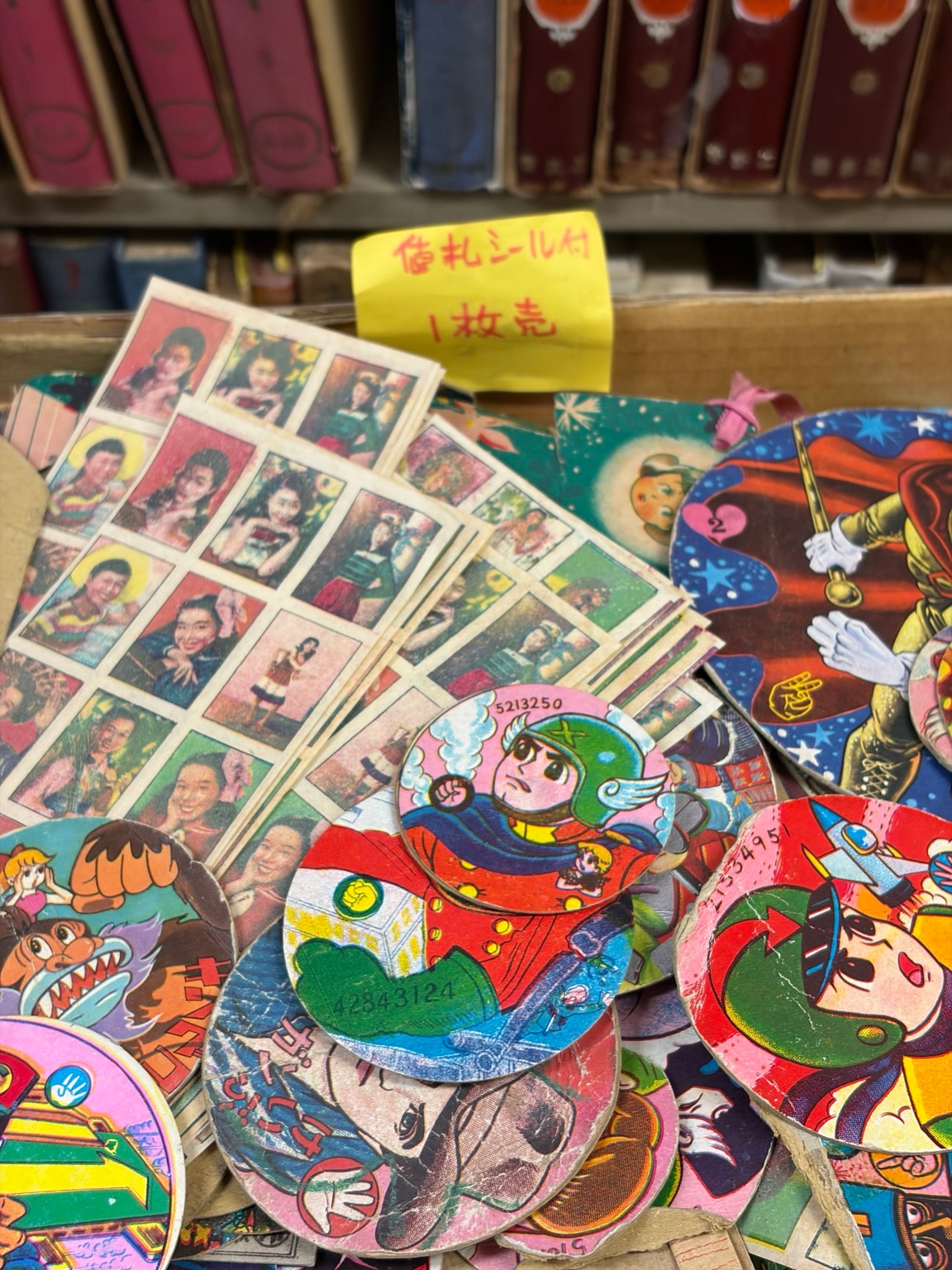 Colourful round paper collectibles and sheets of printed portraits stacked beside old books.